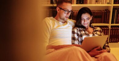 A couple enjoying a cozy evening reading together on a tablet in a home library, symbolizing quiet connection and understanding different social needs in relationships.