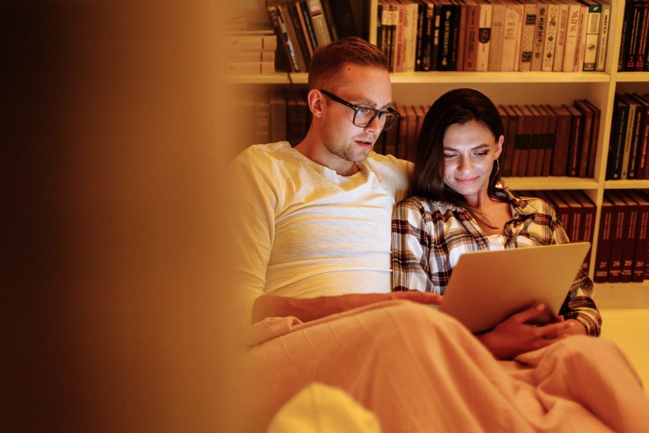 A couple enjoying a cozy evening reading together on a tablet in a home library, symbolizing quiet connection and understanding different social needs in relationships.
